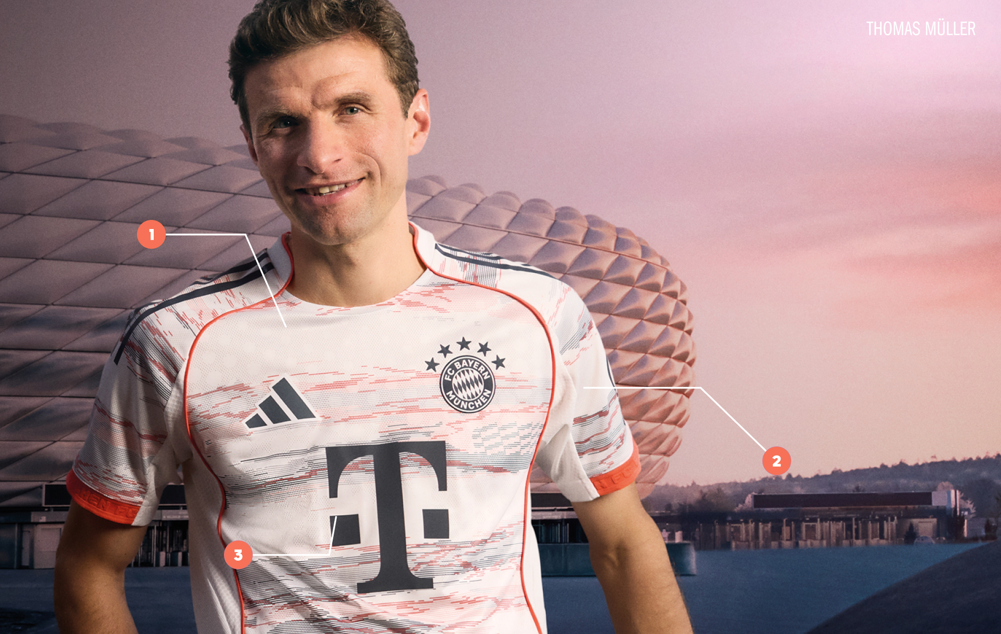 The image shows a smiling man wearing a white and orange soccer jersey with the Bayern Munich logo, standing in front of a backdrop of a stadium or arena.